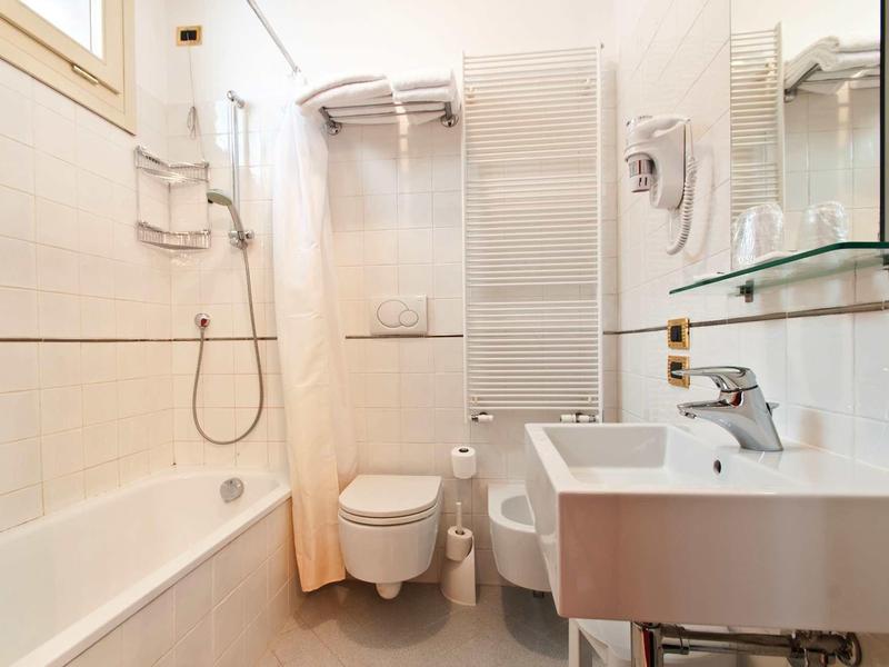 Salle de bain moderne et lumineuse avec baignoire, toilettes, lavabo et sèche-serviettes chauffant.