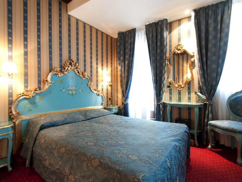 Chambre d'hôtel élégante avec lit baroque bleu, décorations dorées et tapis rouge.