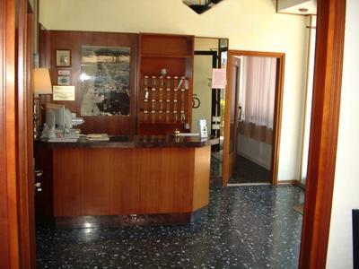 Malá hotelová recepce s dřevěným pultem a skříňkami na klíče na zdi.