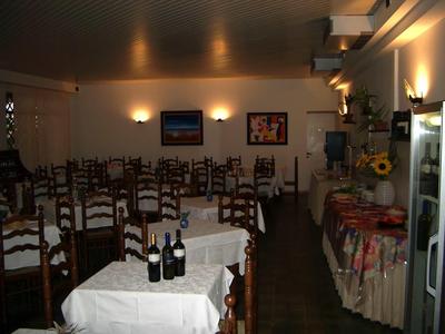 Jídelna s prostřenými stoly, židlemi, lahvemi vína a stěnami zdobenými obrazy.