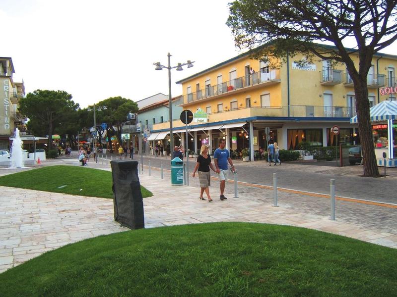 Lidé chodí po dlážděných ulicích poblíž restaurací a obchodů se stromy ve městě.