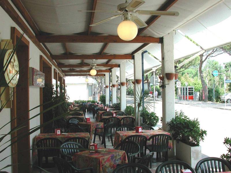 Zastřešené posezení venku s stolky a židlemi vedle ulice v oblasti hotelu nebo restaurace.