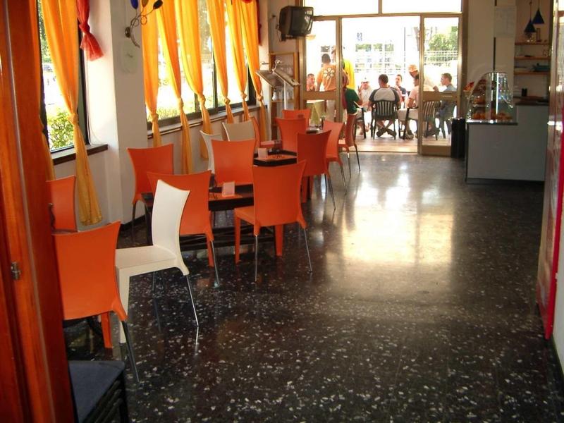 Dlouhá místnost s oranžovými a bílými židlemi, stoly a velkými okny v hotelové restauraci.