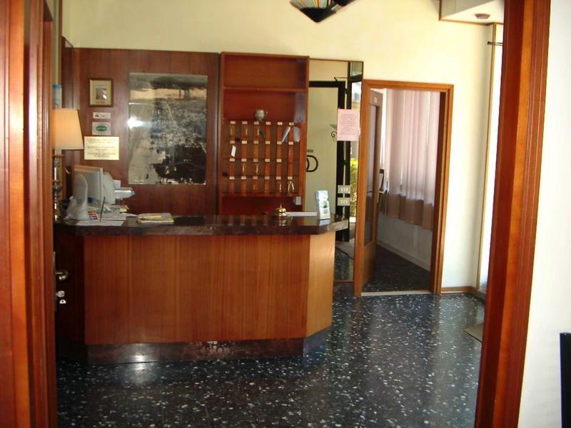 Malá hotelová recepce s dřevěným pultem a skříňkami na klíče na zdi.