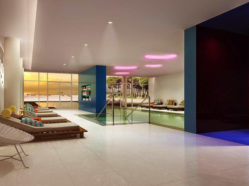 Moderní vnitřní bazén s lehátky, velkým oknem a barevnými průhlednými stěnovými panely.