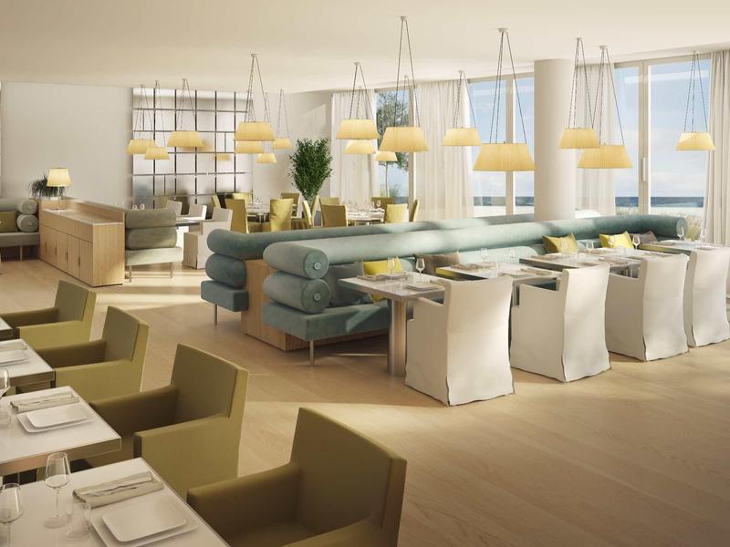 Světle moderní restaurace s béžovými a modrými sedadly a závěsnými lampami nad stoly.