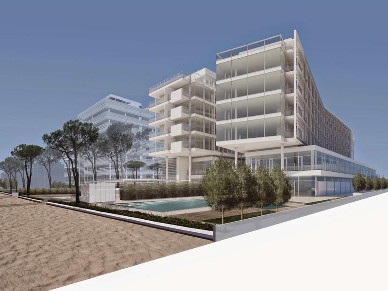 Moderní vícepodlažní hotel s prosklenou fasádou u pláže pod jasnou modrou oblohou.