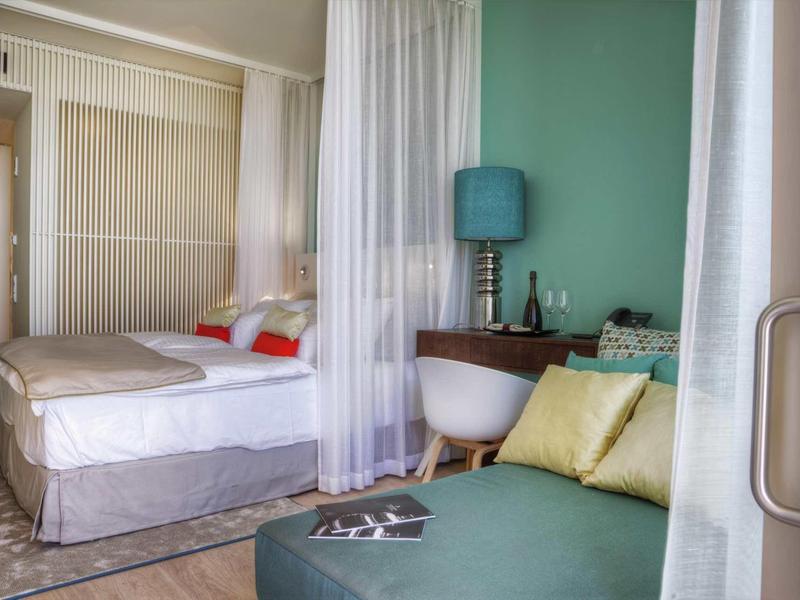 Moderně zařízený hotelový pokoj s postelí, posezením a závěsy pro soukromí.