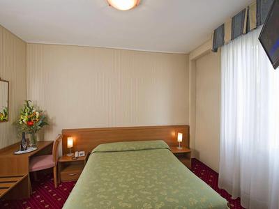 A simply furnished hotel room with a single bed, table, chair, and wall-mounted TV.