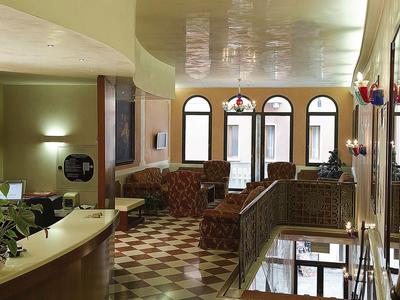 Einladender Hotelkorridor mit Empfangstresen, Ledersesseln, Bogenfenstern und kariertem Boden.