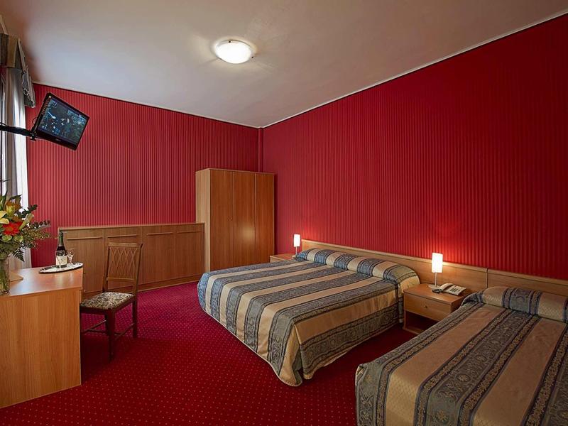 Hotel room with red wall, two beds, wardrobe, and desk with chair.