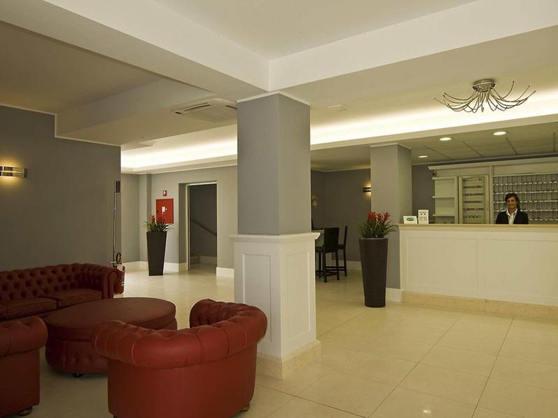Hotel lobby with red sofas, reception desk, and bright lighting.