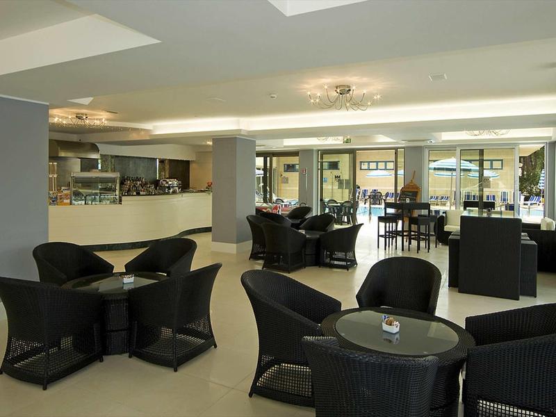 Modern hotel lounge with black chairs and tables in a bright room with large windows.
