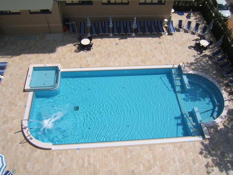 Large rectangular pool with adjacent hot tub and sun loungers in the shade.