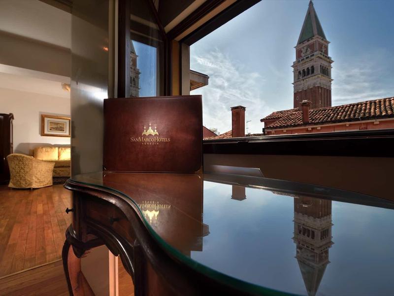 Výhled z hotelového pokoje na stůl, židli a věž na pozadí při západu slunce.