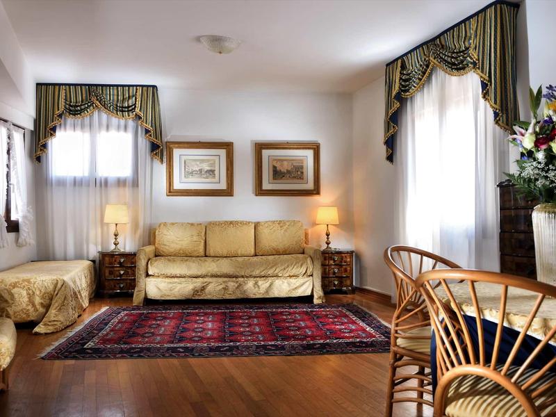 Elegantní obývací pokoj s béžovou pohovkou, dřevěnou podlahou a červeným kobercem v světlém prostoru.