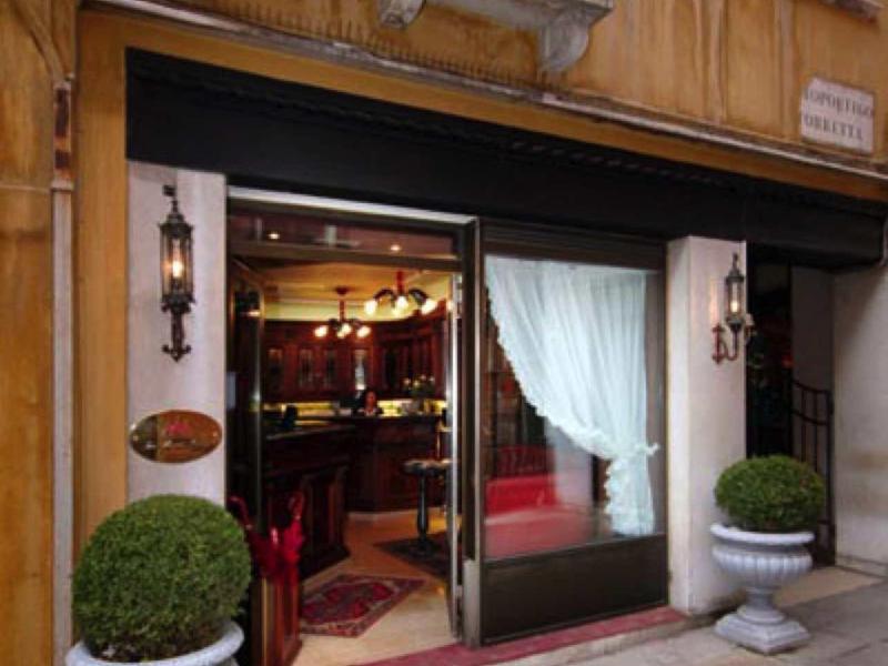 Vstup do elegantního hotelu s velkými skleněnými okny a dekorativními rostlinami.