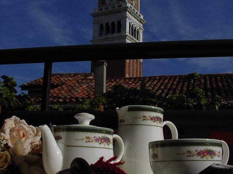 Čajová souprava s šálky, konvicí a věží v pozadí pod jasnou oblohou.