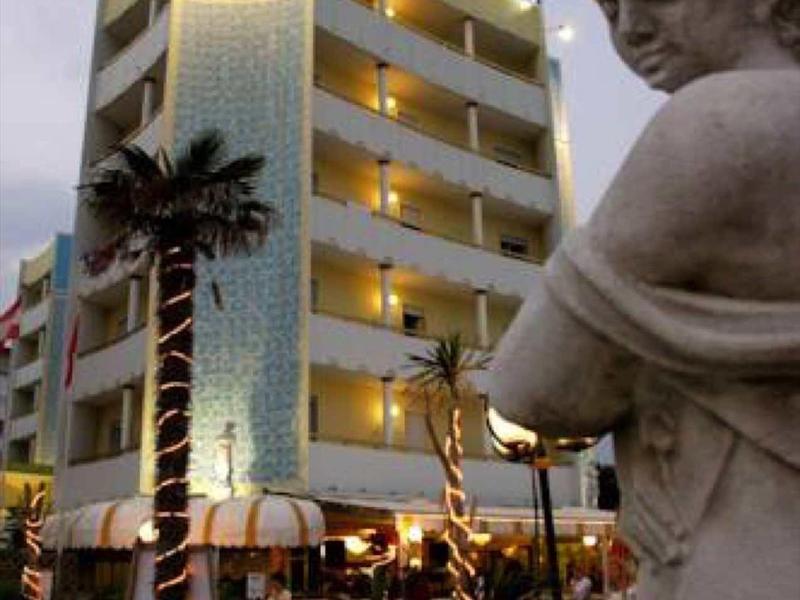 Evening view of a multi-story hotel with illuminated facade, palm trees, and a cherub statue