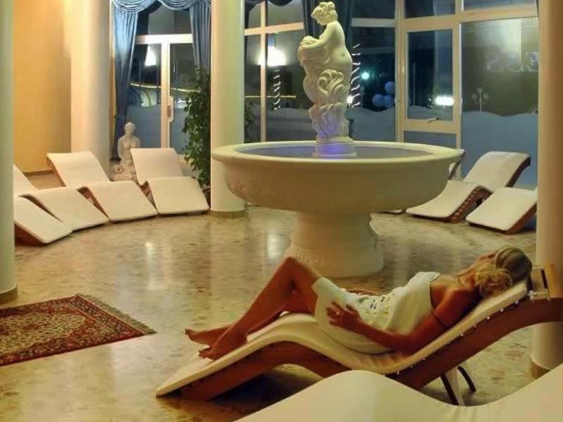 Elegant relaxation room with loungers, fountain, and chandelier in a spa area.