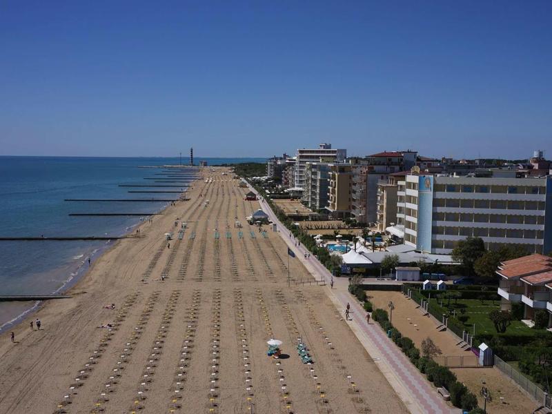 Expansive beach with rows of umbrellas next to a coastal hotel under clear skies.