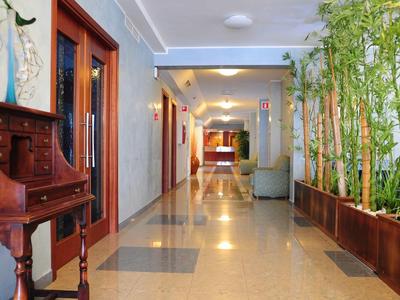 Corridoio d'hotel con piante e mobili in legno, ben illuminato e pulito.