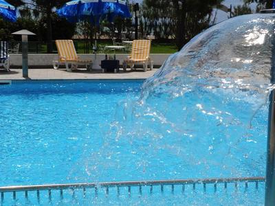 Piscina limpida con cascata e ombrelloni blu sullo sfondo in una giornata di sole.
