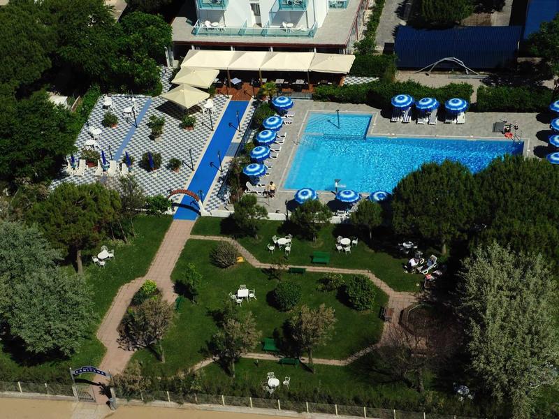 Vista di una piscina dell'hotel con lettini, ombrelloni e un'area giardino adiacente.