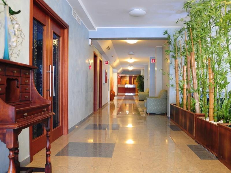 Corridoio d'hotel con piante e mobili in legno, ben illuminato e pulito.