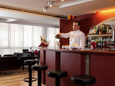 Barman podává nápoje ve stylovém hotelovém baru s barovými židličkami a útulnou lounge atmosférou.