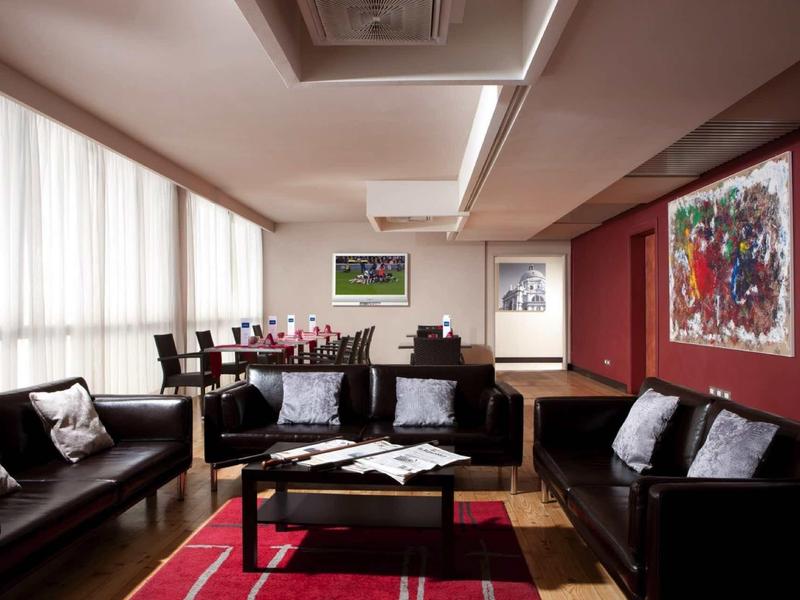 Moderně zařízený obývací pokoj s černými pohovkami, červeným kobercem a velkými okny.