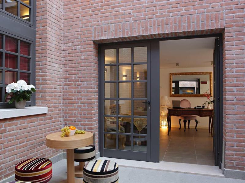 Przytulne miejsce do siedzenia z drewnianymi stołkami i stołem przed otwartymi drzwiami prowadzącymi do jasnego wnętrza.