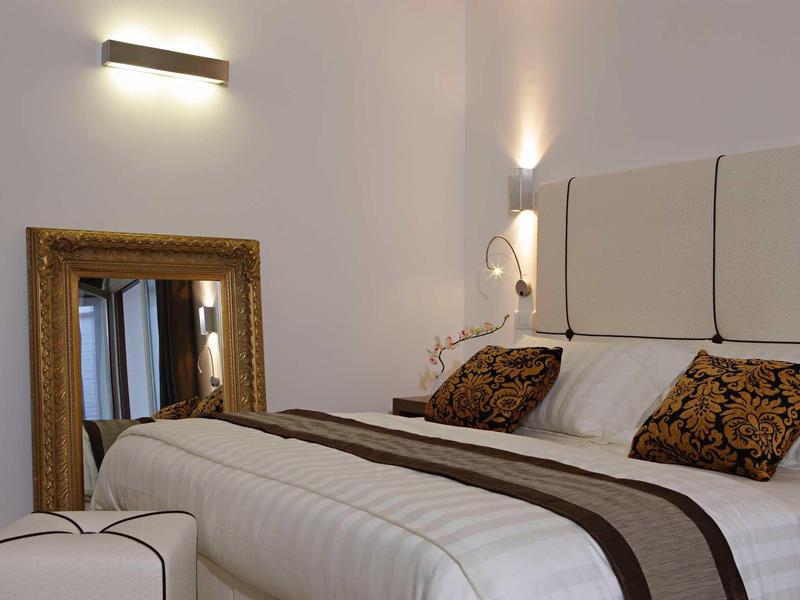 Nowoczesna sypialnia z białym łóżkiem, ozdobiona brązowymi poduszkami i elegancką ramą lustra.