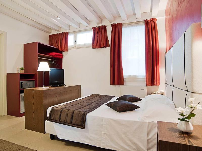 Nowoczesny pokój hotelowy z podwójnym łóżkiem, biurkiem i czerwonymi zasłonami w oknach.