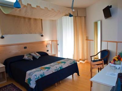 Helles Schlafzimmer mit Doppelbett, Holzboden, Sessel, Schreibtisch und Balkon mit Gardinen.