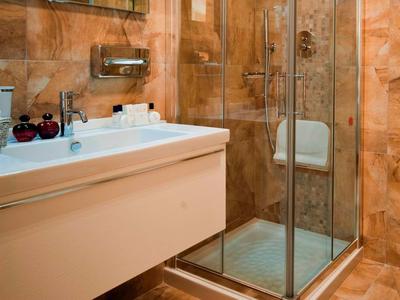 Modernes Badezimmer mit beiger Marmoroptik, Glasdusche und weißem Waschbecken mit Unterschrank.