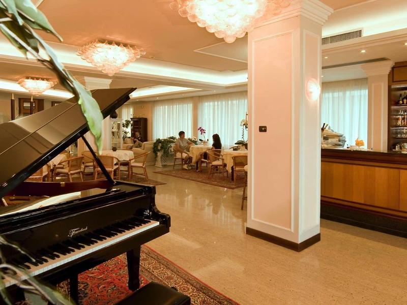 Eleganter Hotel-Lobby mit schwarzem Flügel, Marmorboden und Bar im warmen Licht.