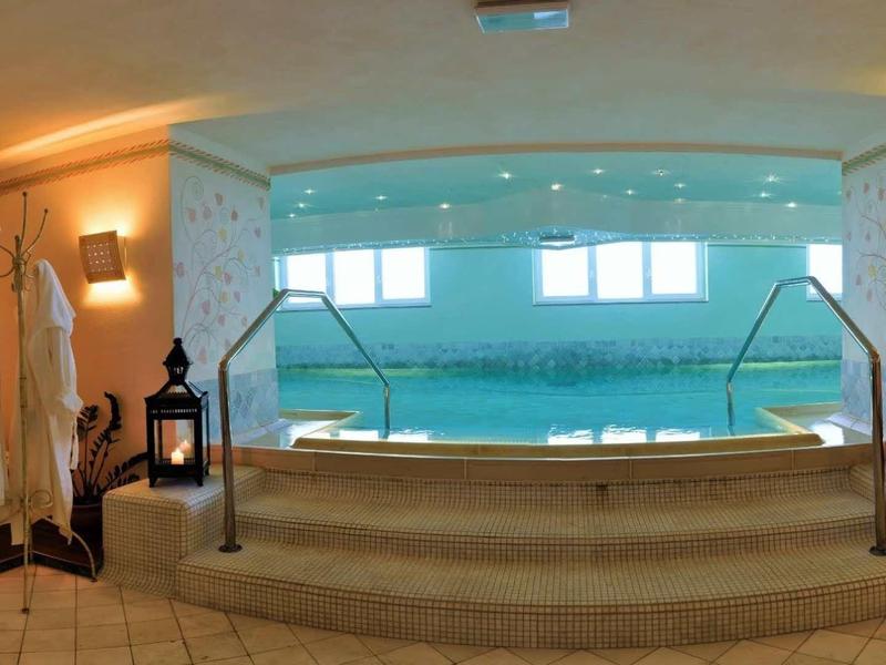 Innenraum mit großem beheiztem Pool, Treppen, weißen Bademänteln und stimmungsvoller Beleuchtung.