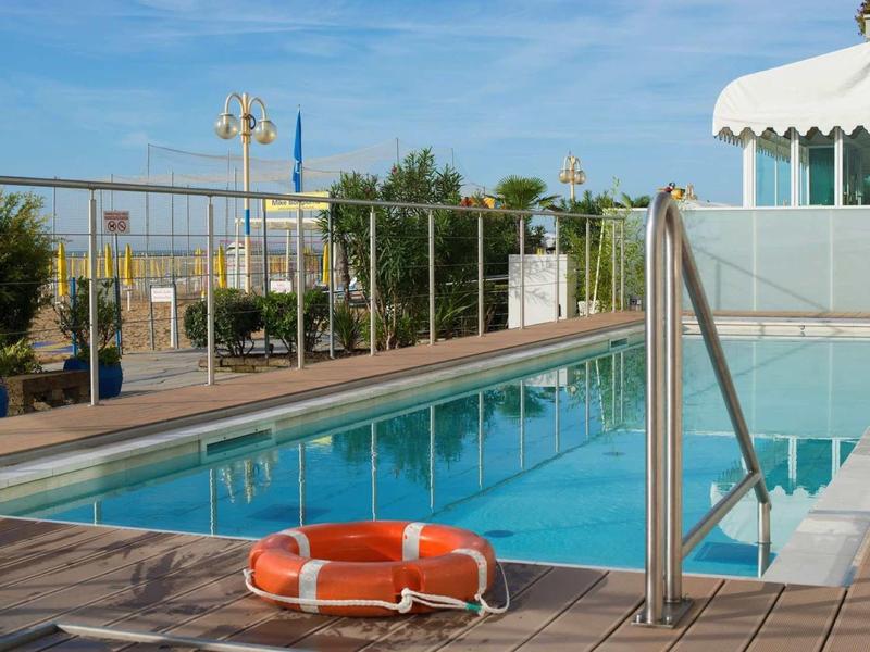 Schwimmbecken mit klarem Wasser, Metallgeländer, orangener Rettungsring auf Holzdeck.