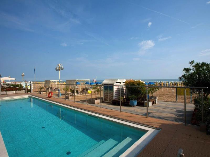 Freier Swimmingpool mit klarem Wasser, Poolbereich mit Stühlen, sichtbarer Strand und blauer Himmel.