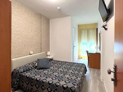 Small hotel room with double bed, flat-screen TV, and window with curtains.