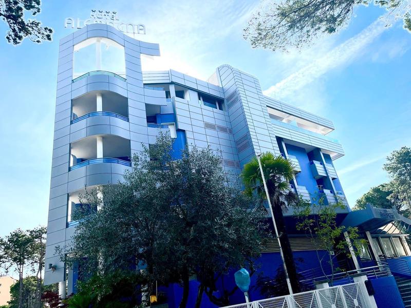 Modern multi-story hotel building with silver facade and blue windows under clear sky.