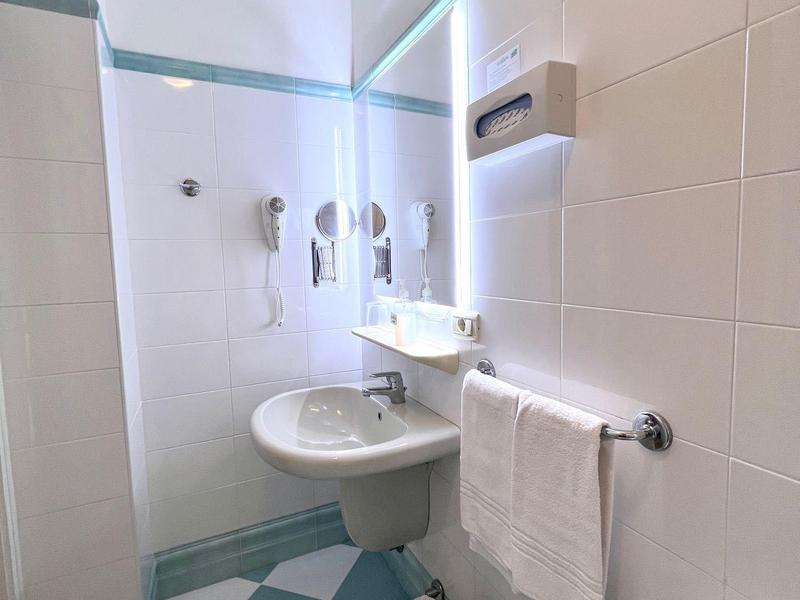 Clean hotel bathroom with washbasin, bidet, toilet, and wall hooks on blue and white floor.