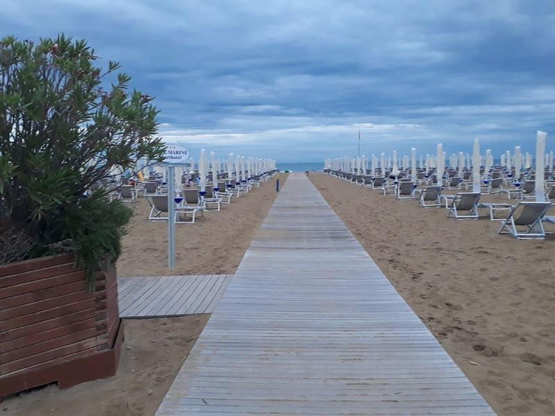 Wooden path leads through sandy beach with rows of umbrellas and loungers under cloudy sky.