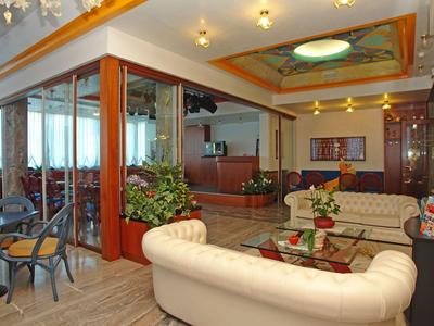 Helle Hotellounge mit weißen Ledersofas und Glas-Couchtischen, neben einem Sitzbereich mit Stühlen.