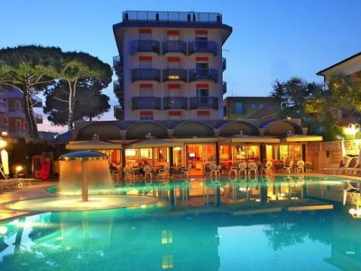 Beleuchteter Swimmingpool mit Liegestühlen und Hotelgebäuden im Hintergrund bei Abenddämmerung.