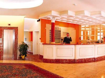 Helle Hotellobby mit Rezeption, Teppich, Aufzügen und dekorativen Pflanzen