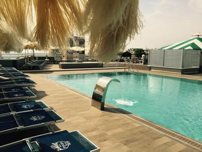 Moderner Hotelpool mit blauen Liegestühlen und Wasserfallfontäne unter Sonnenschirmen.