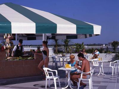 Menschen sitzen unter markant gestreiftem Sonnenschirm auf Hotelterrasse bei sonnigem Wetter.