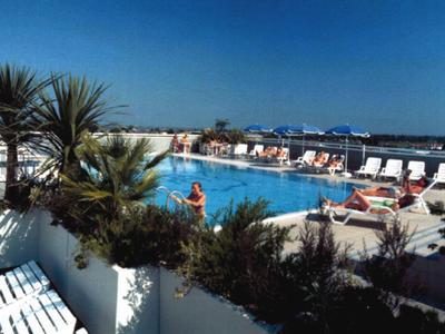 Ein Außenpool mit Liegestühlen, Pflanzen und Blick auf das Meer bei klarem Himmel.